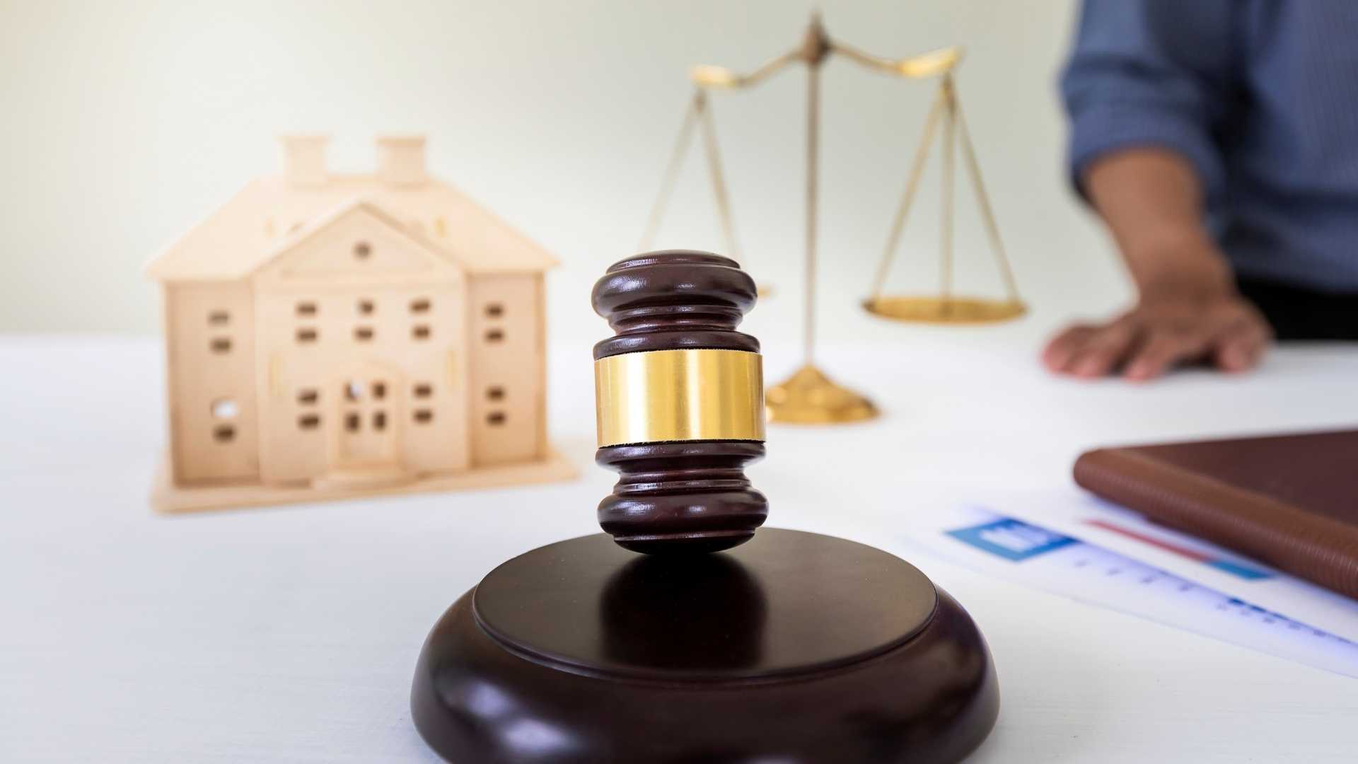 a judges gavel, a home figurine and a legal balance on a white table